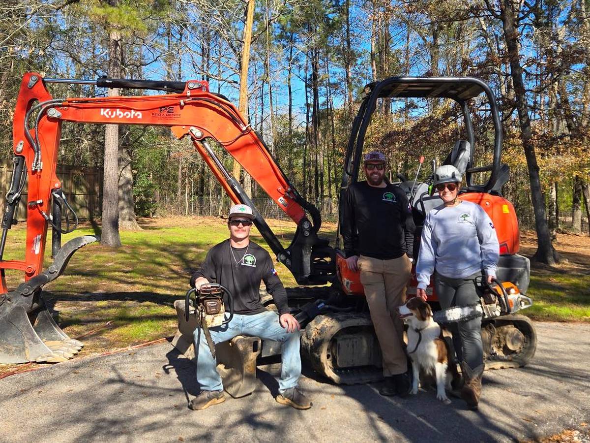 The Branching Out Arboreal crew and their dog with a Kubota mini excavator on a wooded job site near Huntsville, TX